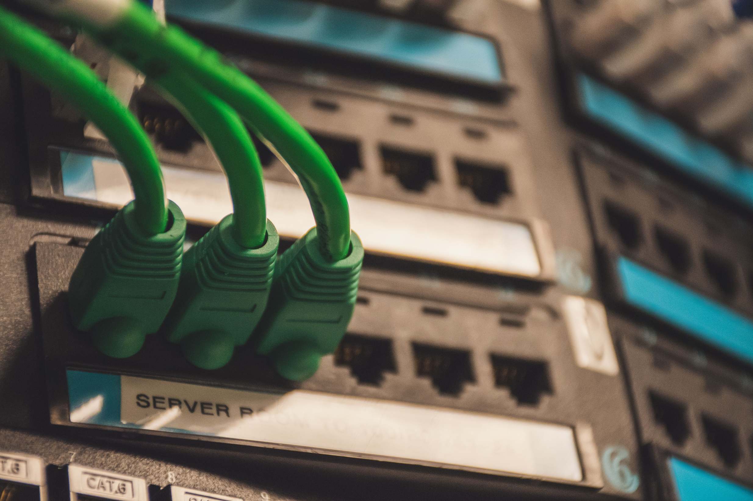 อุปกรณ์เครือข่ายและเซิร์ฟเวอร์ในห้องศูนย์ข้อมูล — Close-up of green network cables plugged into server ports, showcasing technology setup.