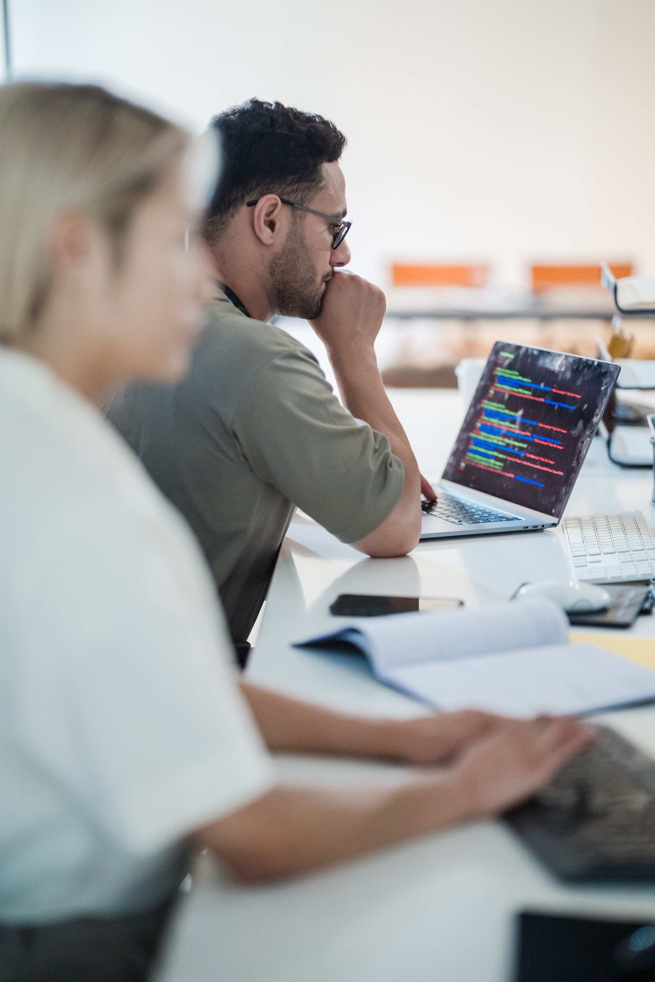 โต๊ะทำงานพัฒนาแอปบนแล็ปท็อป — Two software developers work collaboratively on a coding project in a modern office setting.